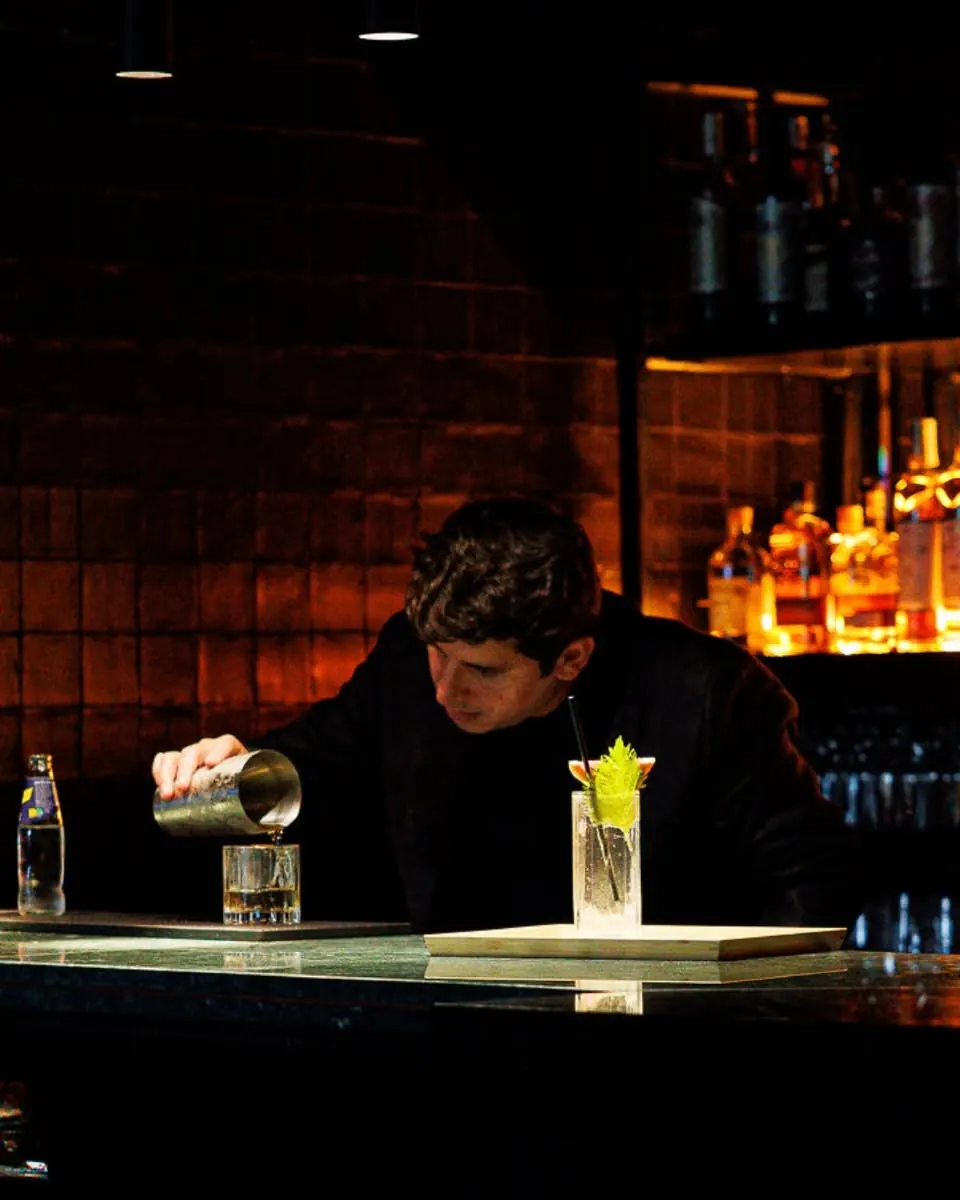 A bartender preparing a cocktail at the backlit bar