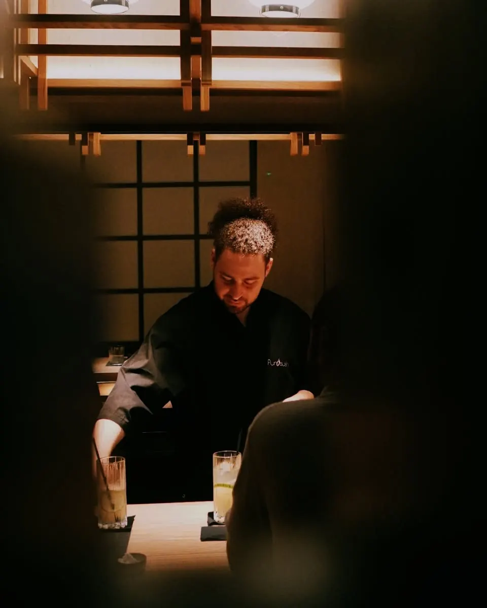 A sushi chef working behind the counter, seen between two guests
