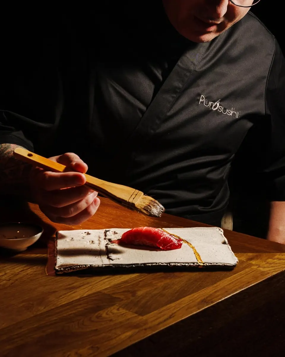A chef brushing glaze over tuna nigiri on a ceramic plate