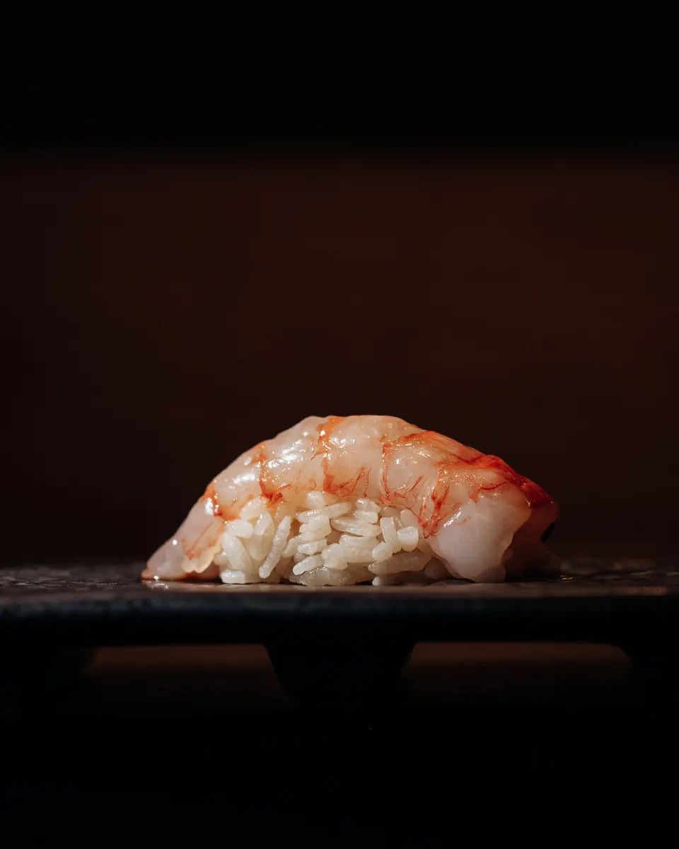 Red prawn nigiri against a dark background