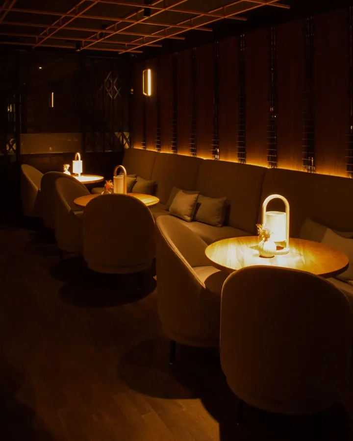 Lounge tables lit by small lamps along an upholstered banquette