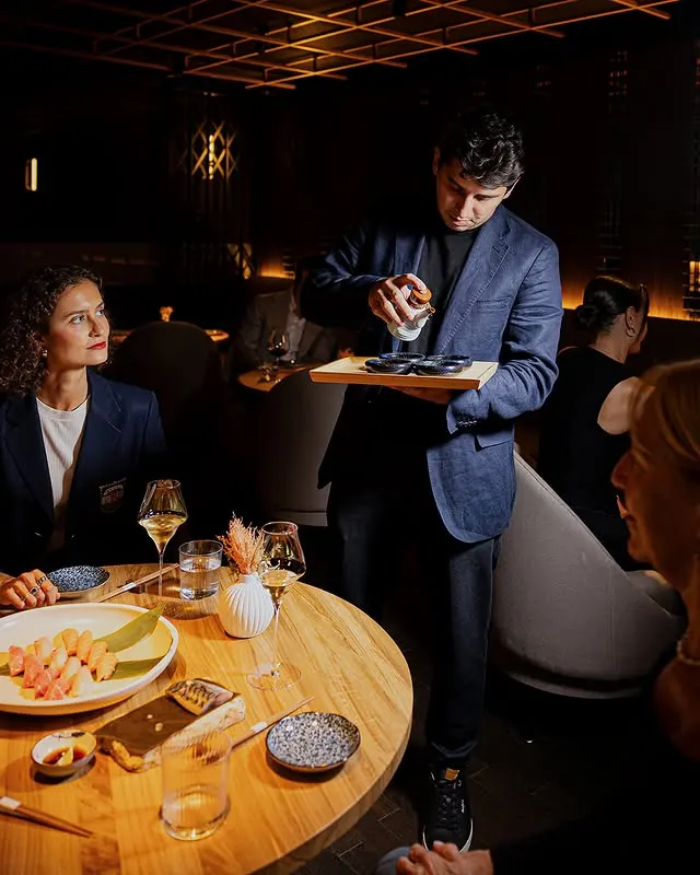 A host serving guests at a round Lounge table