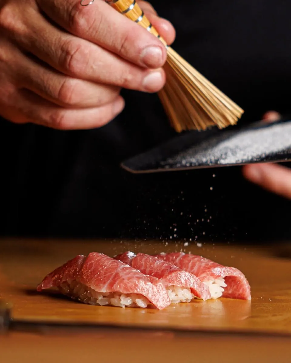 A chef brushing salt over fatty tuna nigiri