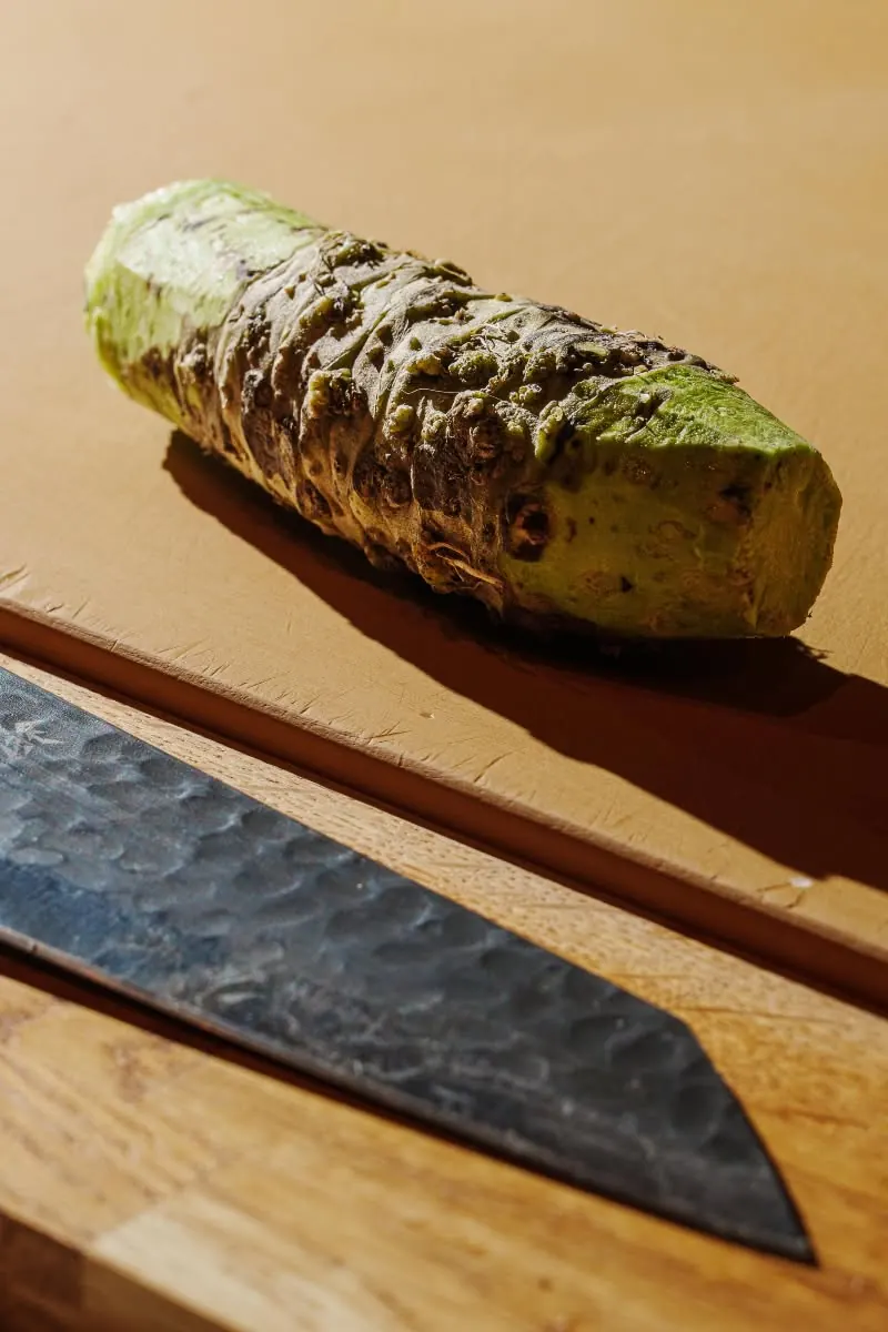 Fresh wasabi root beside a hammered knife blade